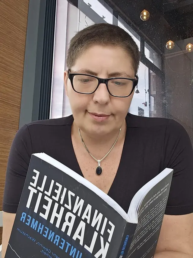 Sina Riegel mit Brille beim Lesen eines Buches über finanzielle Klarheit für Unternehmer
